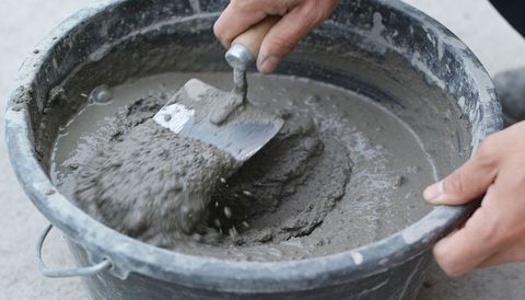 Contractor mixing mortar with trowel in bucket closeup, hands working on concrete repair
