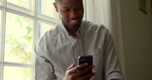 Smiling Man Using Smartphone by Bright Window - Download Free Stock Photos Pikwizard.com