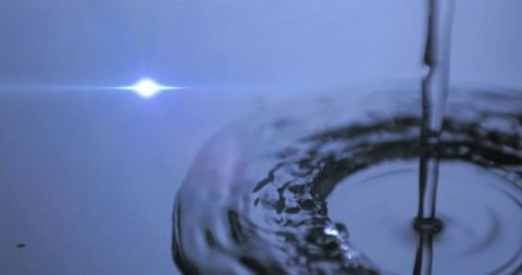 Pouring water creates ripples on reflective surface with lens flare