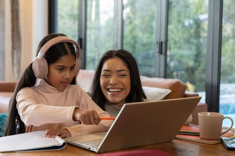 Mother helping daughter with remote learning on laptop, pointing and smiling