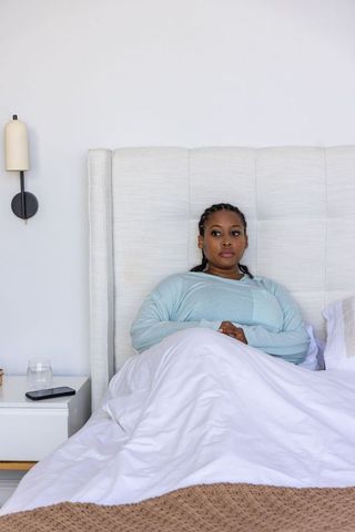 African american woman relaxing in minimal neutral bedroom with tufted headboard