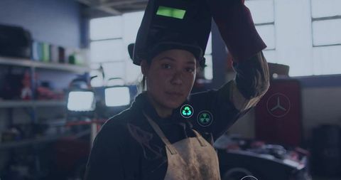 Confident Female Welder Holding Helmet in Busy Workshop