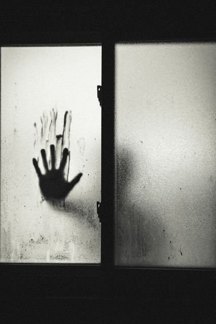 Mysterious silhouette standing behind foggy glass window, handprint clearly visible. Evokes feelings of suspense and fear, ideal for horror themes. Can be used in promotions for Halloween events, horror movies, thriller book covers, or creating spooky, unsettling atmosphere in digital and print marketing campaigns.