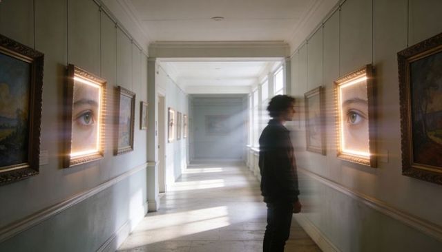 Contemplative man examining glowing eye paintings in sunlit gallery corridor