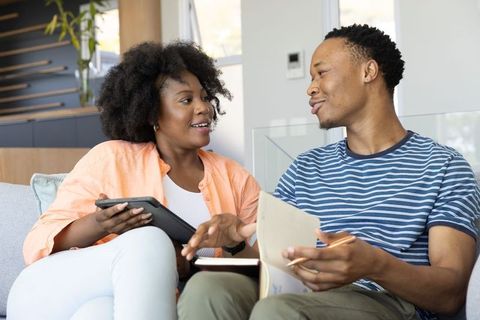 African american couple planning finances at home using tablet and notebook on sofa