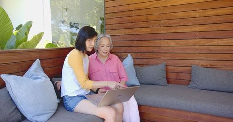 Young woman computing together with senior woman on laptop outdoors