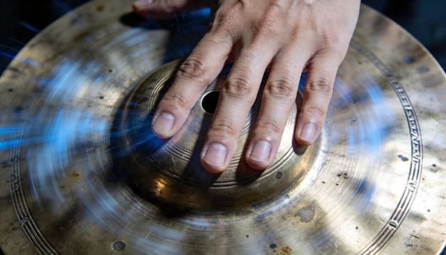 Hand muffling spinning cymbal bell with blue motion blur, close-up percussion macro studio