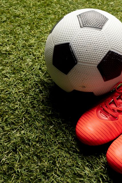 High angle view of soccer ball with red sport shoes over grassy field, copy space. Unaltered, sport and competition concept.