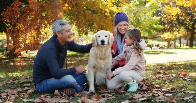 A Caucasian family enjoys a delightful autumn day outdoors with their golden retriever, with copy space. Smiles radiate as the middle-aged man, young woman, and girl share a moment of affection with their pet amidst the fall foliage.