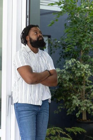 Contemplative man leaning in doorway with folded arms beside lush indoor potted plants