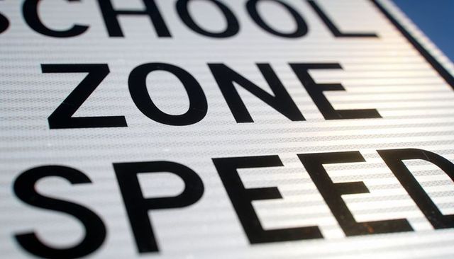Close-up showing school zone speed sign with reflective beads and sun glare on metal