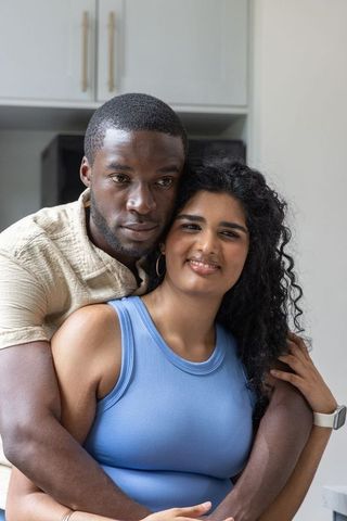 Diverse couple hugging in kitchen, intimate embrace with indian woman in blue tank