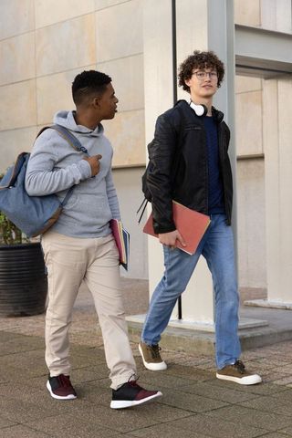 Two teenage male students walking on campus carrying backpacks headphones and notebooks