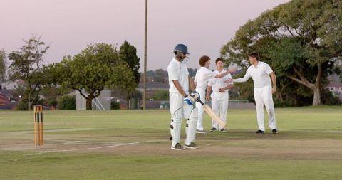 Indian batsman walking off crease at dusk while fielders celebrate wicket