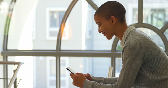 Smiling Young Person Using Smartphone in Modern Room with Arched Window - Download Free Stock Images Pikwizard.com