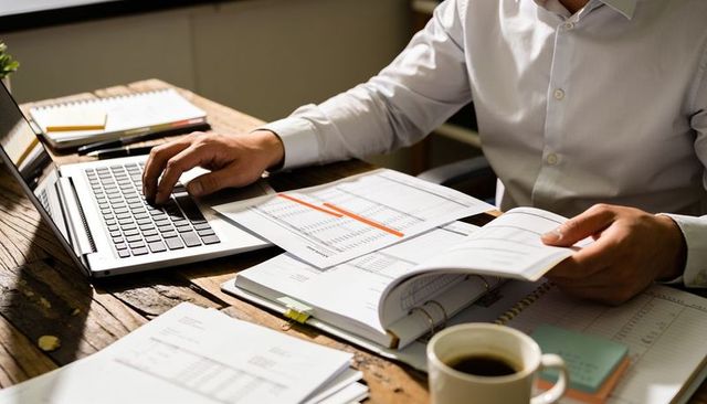 Professional reviewing financial spreadsheets at wooden desk with laptop and coffee