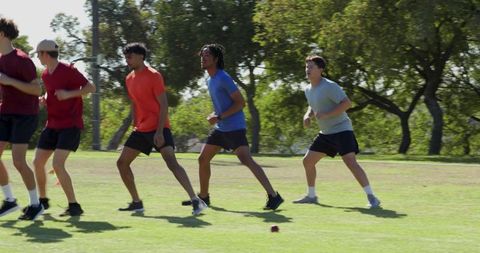 Male athletes side-shuffling during outdoor agility drill on turf field practicing teamwork