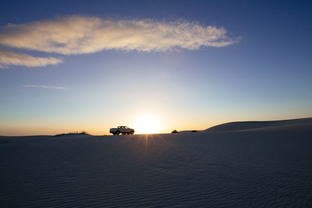 A captivating image of an SUV depicted in silhouette against a stunning sunset in a desert landscape. This visual can be used to emphasize themes of adventure, travel, solitude, and outdoor exploration. It is ideal for travel brochures, adventure blogs, car advertisements, and inspirational posters that focus on road trips and journeys through nature.