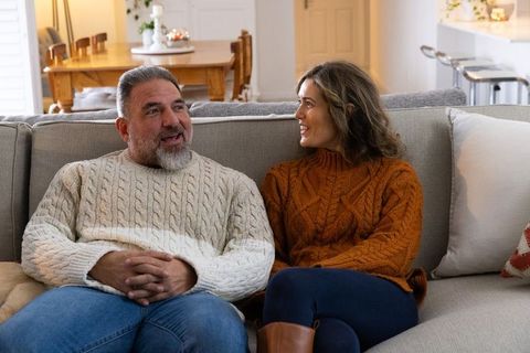 Mature couple relaxing on sofa wearing cozy cable-knit sweaters sharing warm conversation