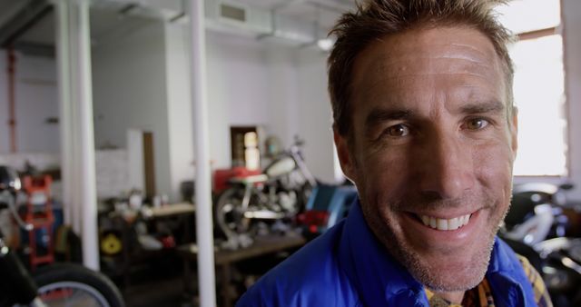 Smiling Man in Industrial Workshop with Motorcycles in Background - Download Free Stock Images Pikwizard.com