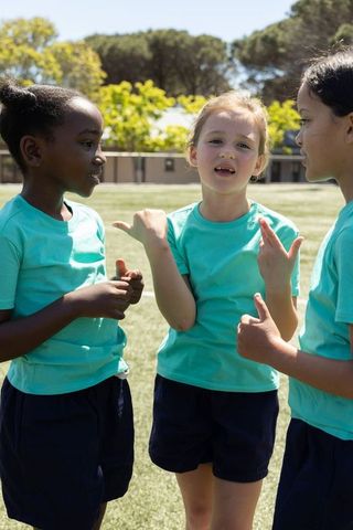 Diverse girls chatting and gesturing on school sports field in teal shirts