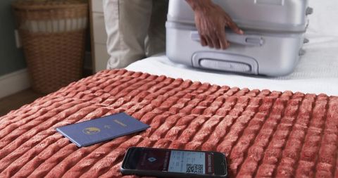 Traveler packing suitcase on bed with passport and smartphone