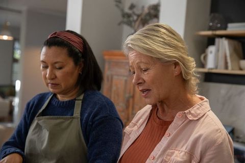Diverse friends preparing meal in cozy kitchen, middle-aged and senior women cooking together