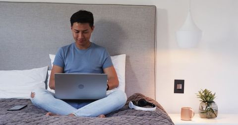 Man Working on Laptop in Cozy Bedroom Environment