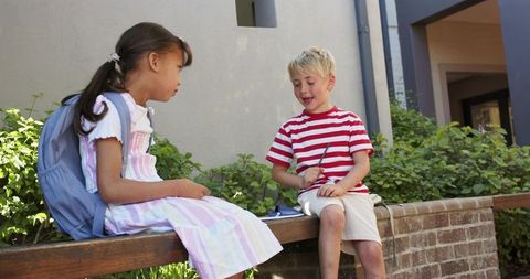 School friends chatting on courtyard wall with backpack and notebook, outdoor learning