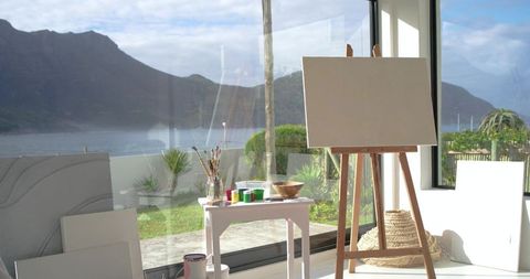 Blank canvas on wooden easel in sunlit coastal studio with ocean view