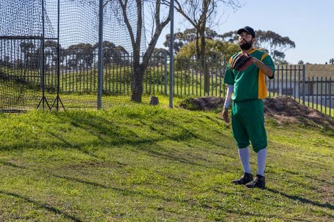 Baseball outfielder standing on grassy field in green uniform holding glove near netting