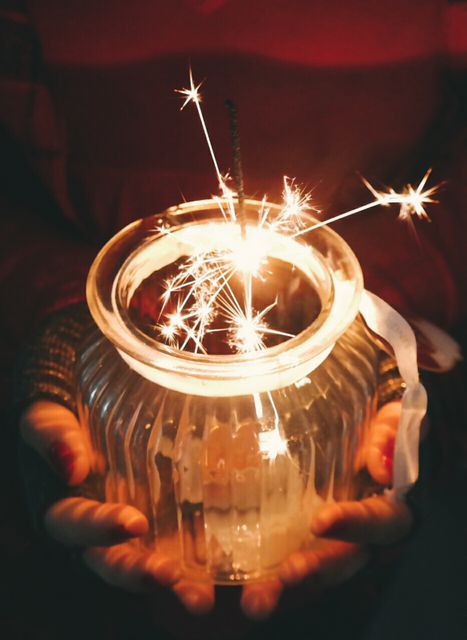Hands clasping jar with sparklers producing festive atmosphere. Ideal for holiday promotions, celebration invitations, party themes, festive greetings, or sparkler safety guides.
