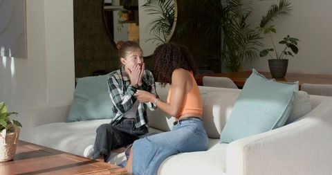 Diverse female couple reacting to surprise in modern living room