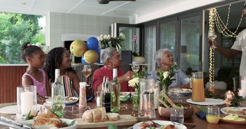 Multigenerational family raising glasses and sharing meal on sunlit covered patio