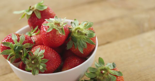 Image depicts a white bowl filled with ripe, red strawberries placed on a wooden table. Ideal for use in health and nutrition content, food blogs, summer recipes, advertisements for fresh produce, and social media promotion of organic fruits.