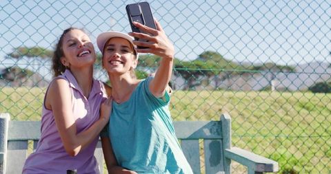 Two women taking selfie on park bench during sunny outdoor break