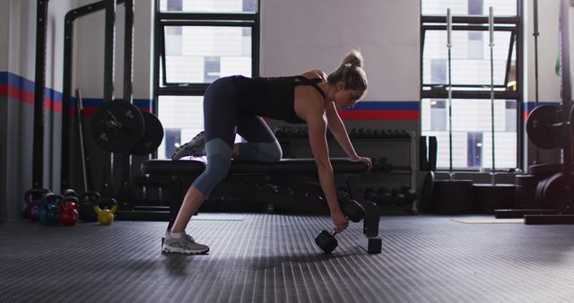 A determined woman in workout gear is performing a dumbbell row exercise, focusing on strength and endurance. Ideal for fitness, health, and gym-related promotions, or use in articles and blogs on strength training, weightlifting techniques, or personal health routines.