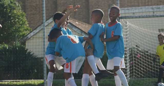 Young soccer players in team uniforms joyfully celebrating a goal during a match on an outdoor field. This image is great for use in materials promoting youth sports, teamwork, emotional moments in sports, and children's activities. It can also be used in advertisements and articles about the benefits of sports for kids and community building through sports.