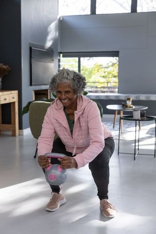 Active senior woman performing kettlebell squat indoors