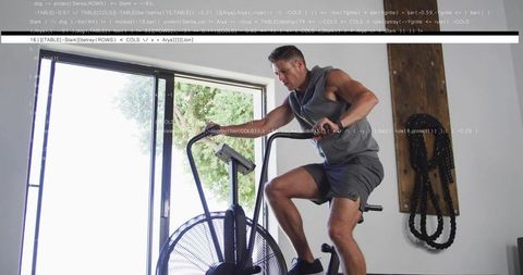Fit man pedaling air bike in home gym during intense cardio training, sunlit interior