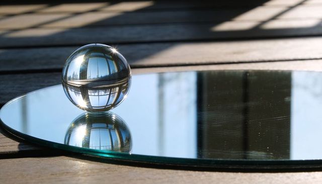 Reflecting crystal sphere capturing inverted window grid on mirror disc over sunlit deck