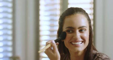 Smiling woman applying makeup in cozy sunlit room