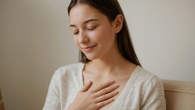 Adult woman placing hand on chest expressing calm gratitude on beige sofa in minimal home