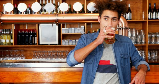 Man Drinking Beer at Bar Counter with Various Bottles in Background - Download Free Stock Images Pikwizard.com