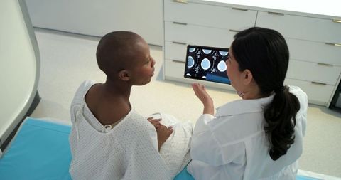 Doctor reviewing brain scans with patient on exam table using tablet during consultation