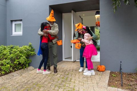 African american family celebrating halloween on porch wearing pumpkin hats and costumes
