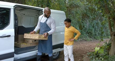 African american father and son unloading wicker crates from white cargo van for local market