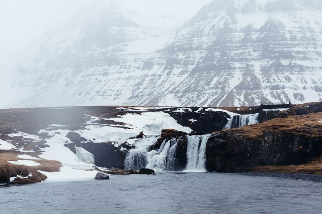 Misty waterfalls amidst snowy mountain scenery, creating a serene and picturesque winter wonderland. This natural landscape exemplifies the beauty of Icelandic wilderness, perfect for travel blogs, tourism marketing, and nature-themed websites.
