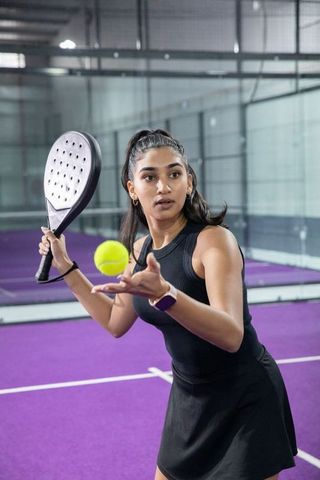 Indian woman serving on purple padel court tossing yellow ball in athletic activewear