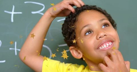 Curious schoolboy touching chin and scratching head at chalkboard with gold stars, dreaming